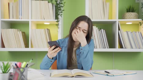 Asian-schoolgirl-studying-at-home-is-upset-about-her-phone-that-runs-out-of-charge.